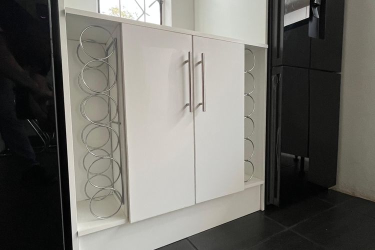 A white base unit with wine racks built into both end panels, between two black fridges