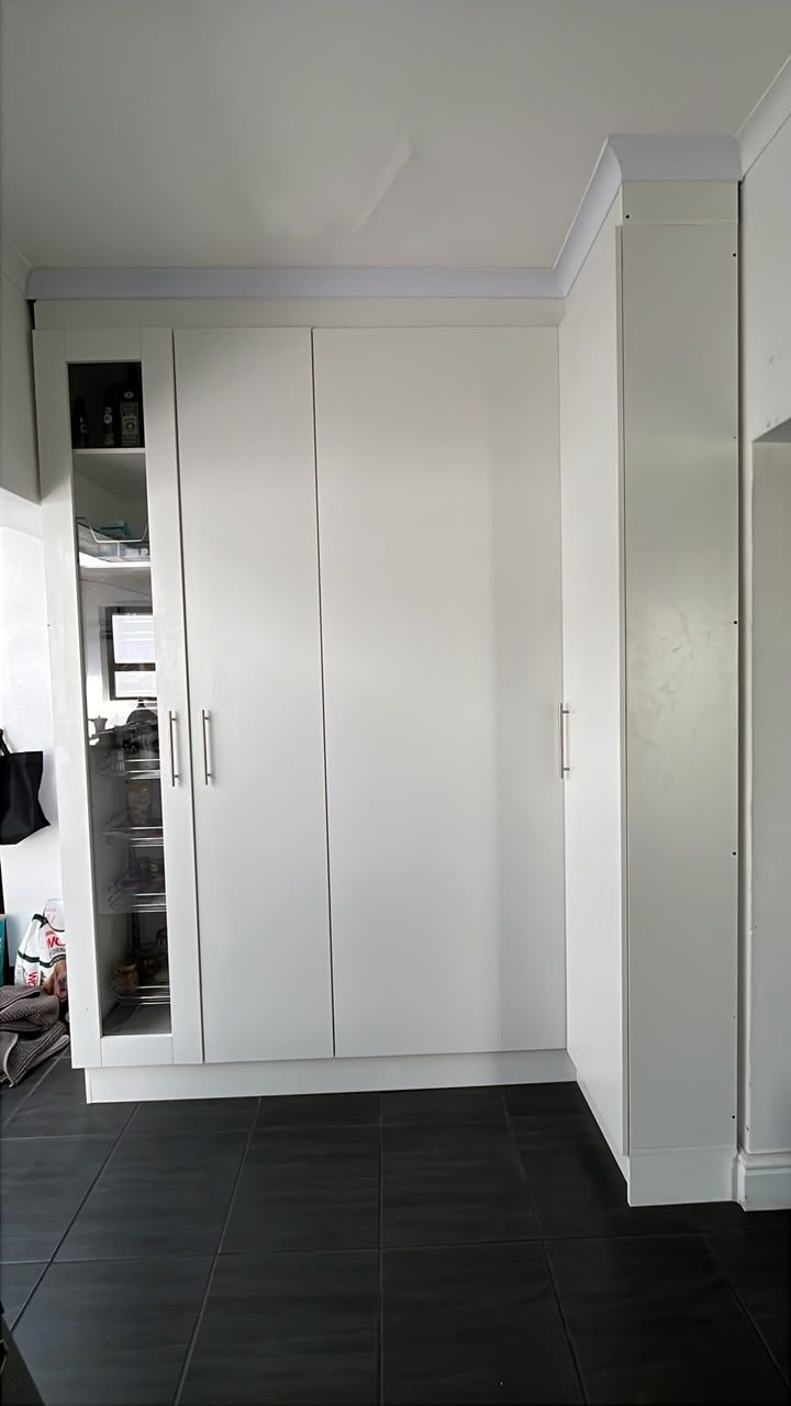 A finished wall of white built-in cupboards with a glass-door pantry