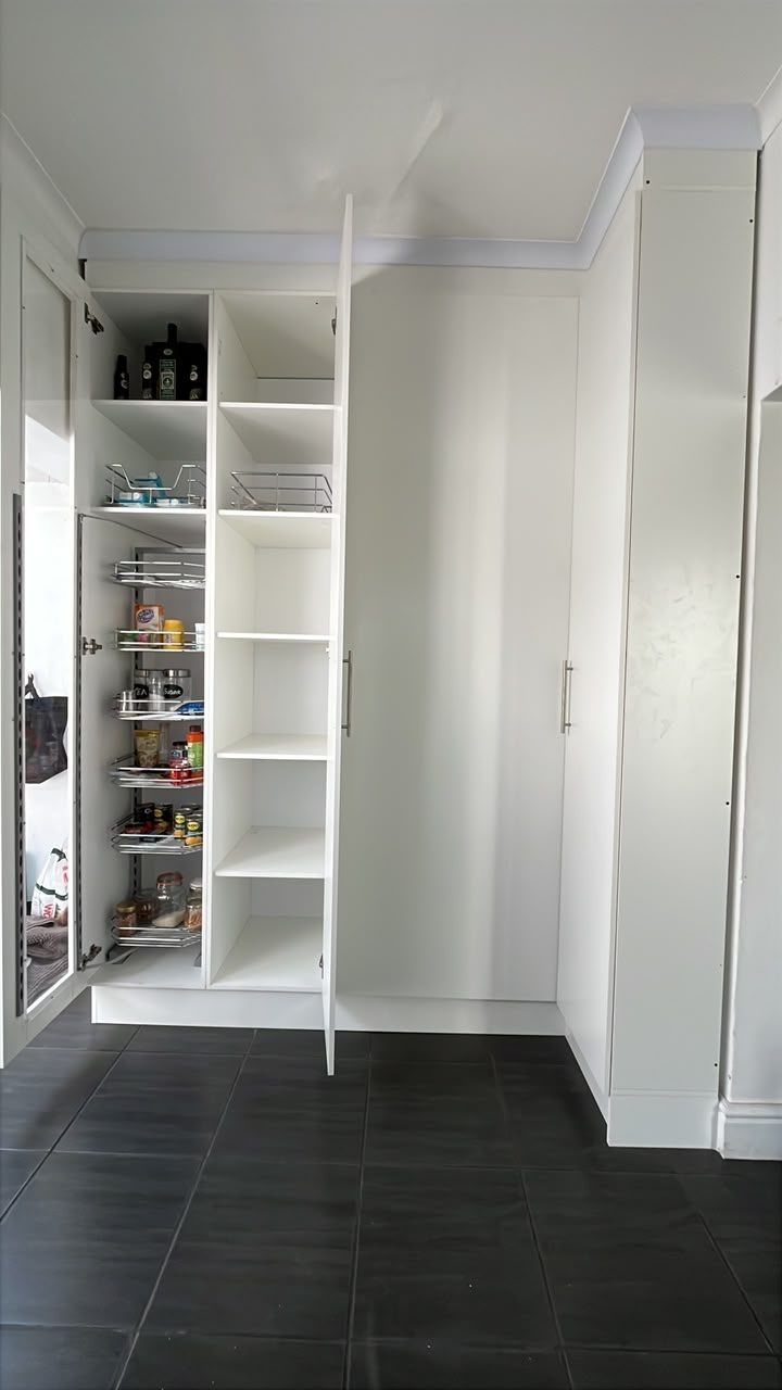 The built-in pantry open: pull-out wire baskets full of tins beside white shelves